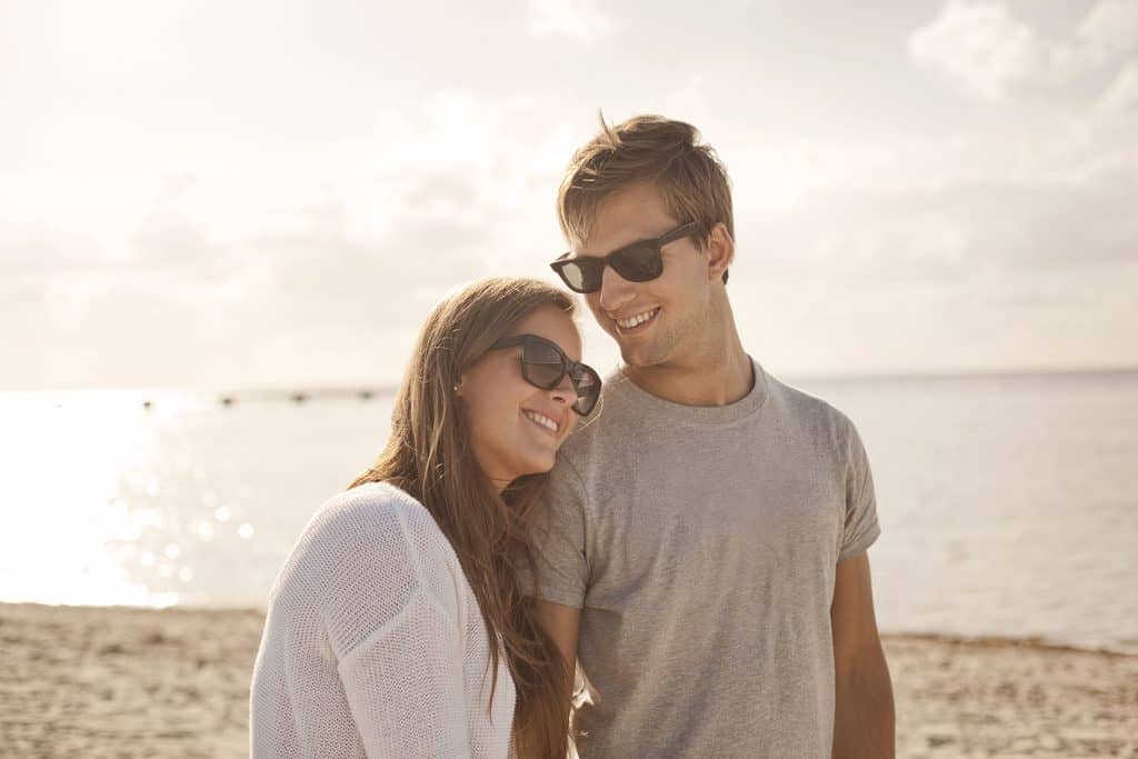 happy couple walking on the beach wearing sunglasses